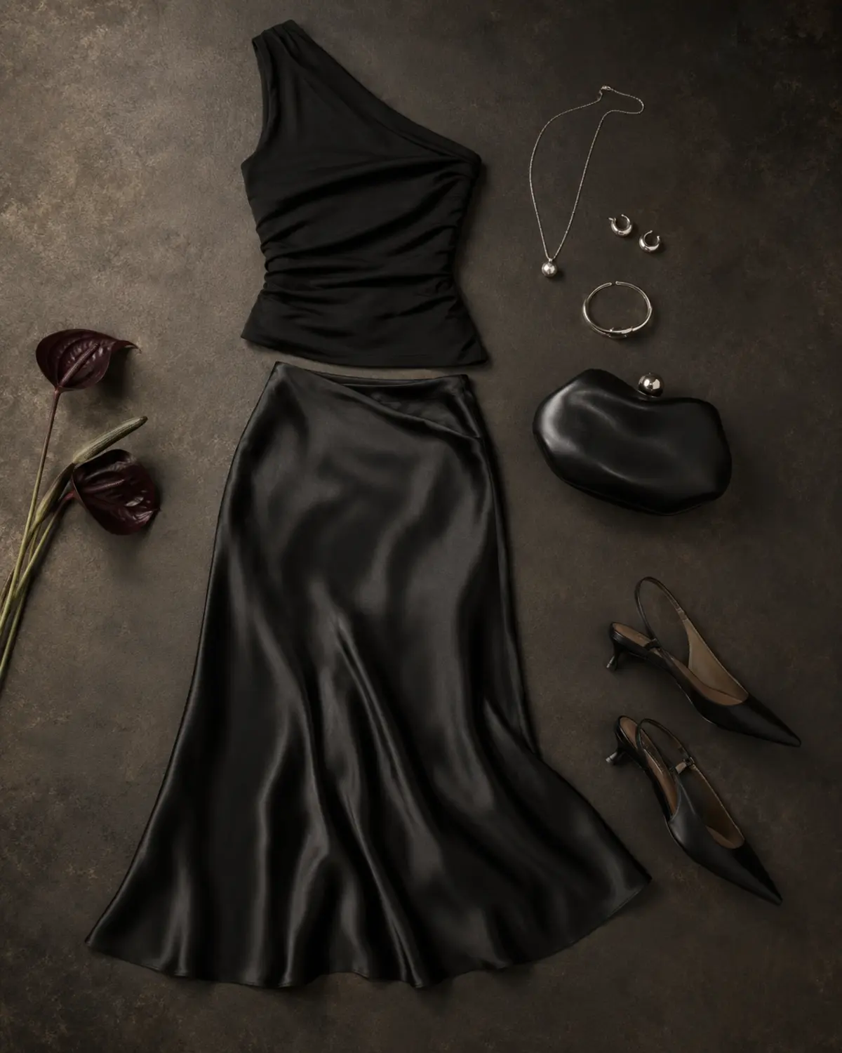 All-black date-night outfit with asymmetric top, satin skirt, heels, clutch, and silver jewelry